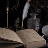 Open journal with a feather pen and crystal ball on a dark background
