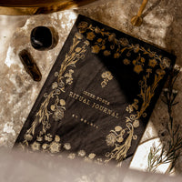 Decorative journal with gold text and designs on a textured surface with crystals.