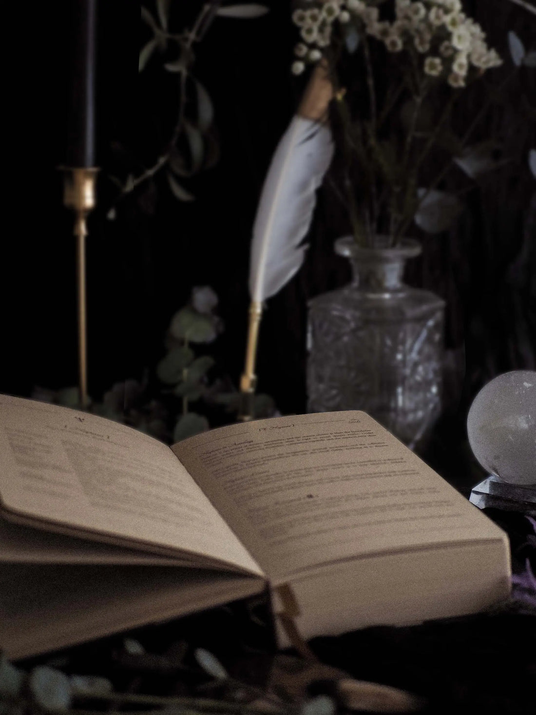 Open journal with a feather pen and crystal ball on a dark background