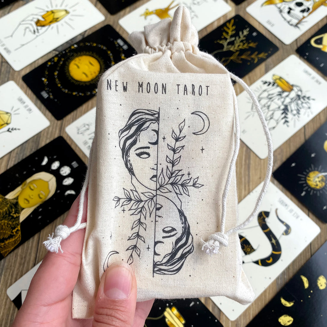 Drawstring pouch labeled 'New Moon Tarot' held over the new moon tarot cards